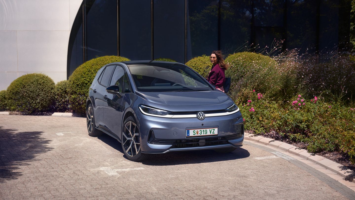 Egy nő áll egy kék VW ID.3 Neo vezetőoldali ajtajánál, az autó egy modern irodaépület előtt parkol.