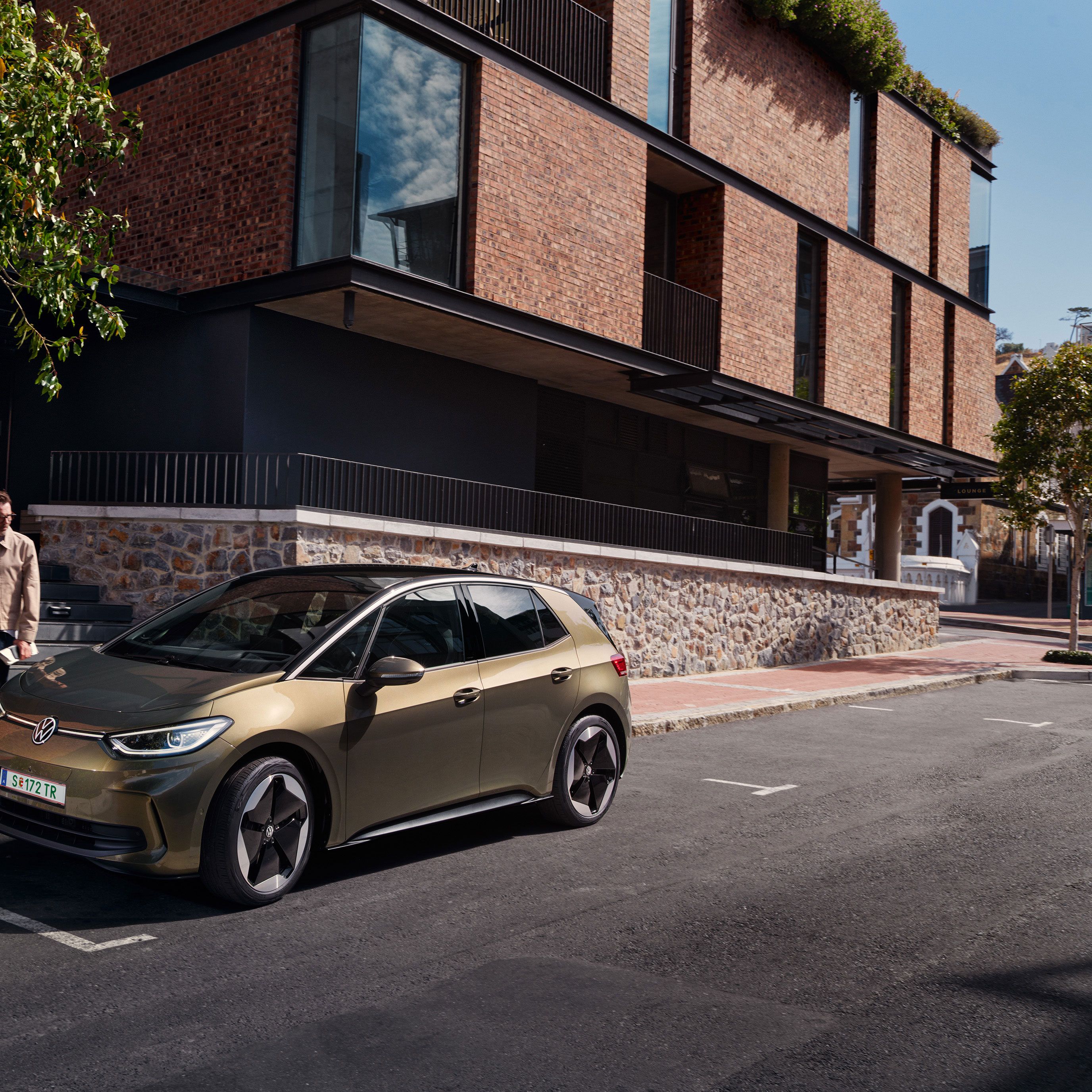Blick auf einen VW ID.3 in "Dark Olivine Green Metallic", der am Straßenrand am Bordstein parkt.