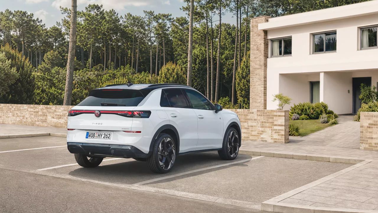 Egy fehér Volkswagen T-Roc Hybrid áll egy erdő melletti lakóház előtti parkolóban, hátulról nézve.