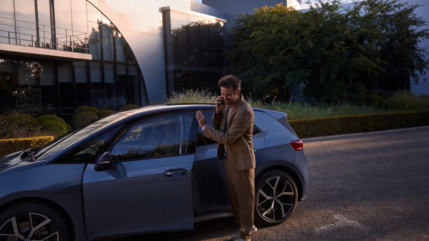 Egy férfi egy kék VW ID.3 Neo előtt áll, és az okostelefonján telefonál.