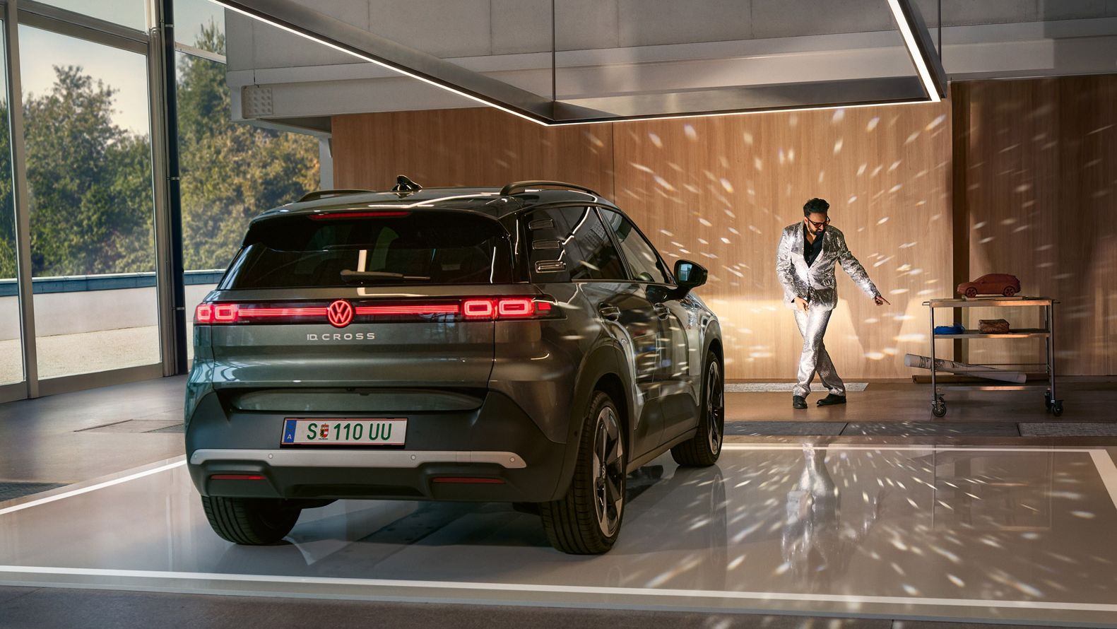 Egy VW ID. Cross bekapcsolt fényszórókkal áll egy csarnokban, és megvilágít egy csillogó öltönyben táncoló férfit.