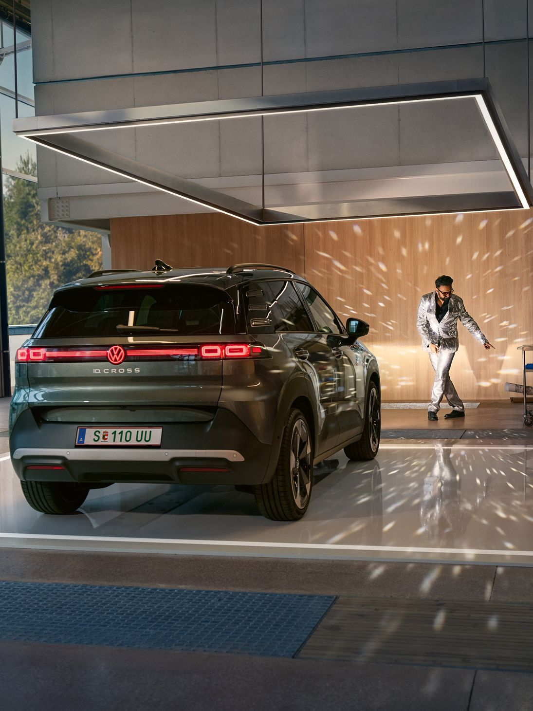 Egy VW ID. Cross bekapcsolt fényszórókkal áll egy csarnokban, és megvilágít egy csillogó öltönyben táncoló férfit.