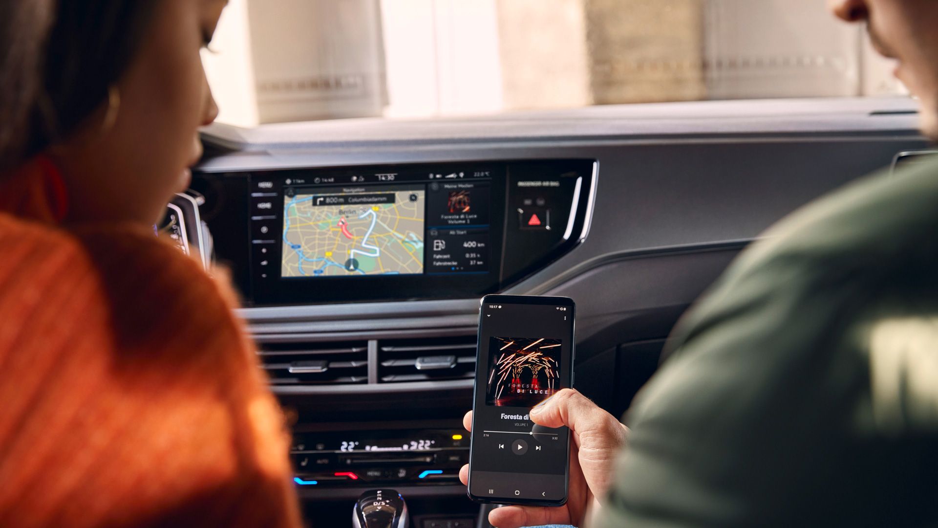 A VW Poloban ketten ülnek, jobbról egy okostelefont tartanak fel, ami vezeték nélkül csatlakozik az infotainment rendszerhez.