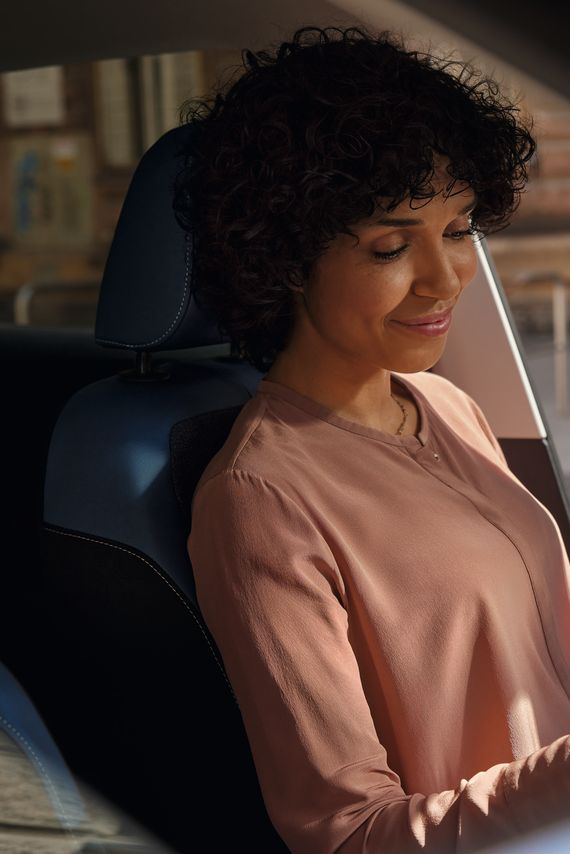 Eine lächelnde Frau schaut auf dem Fahrersitz eines parkenden VW T-Cross aufs Handy.