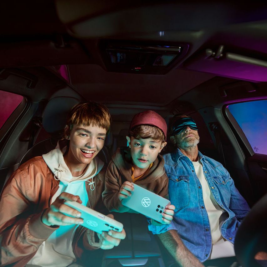 Apa két gyerekkel a Volkswagenben, a gyerekek az AirConsole-lal játszanak.
