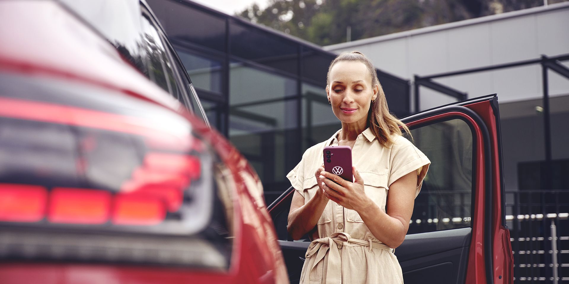 Nő egy VW modell mellett nézi a telefonját