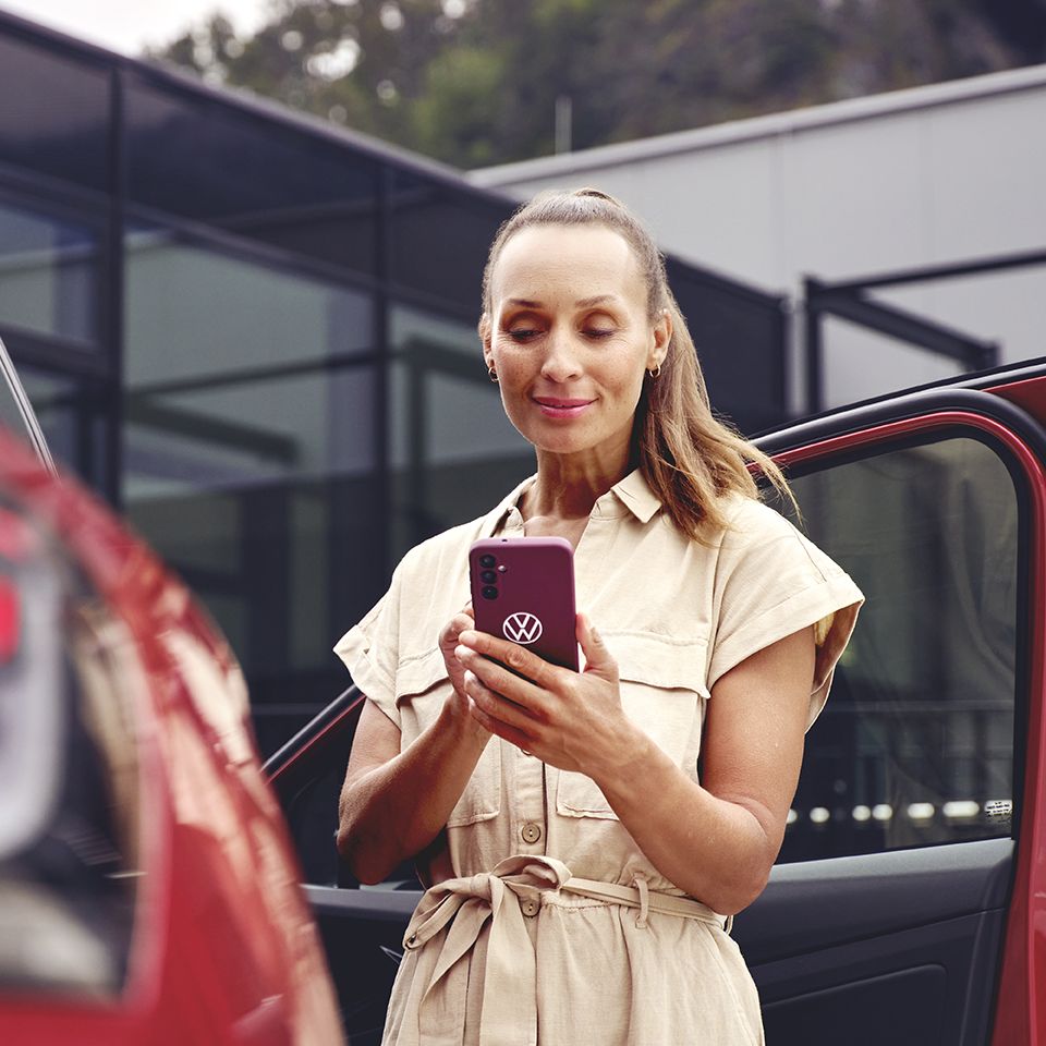 Nő egy VW modell mellett nézi a telefonját
