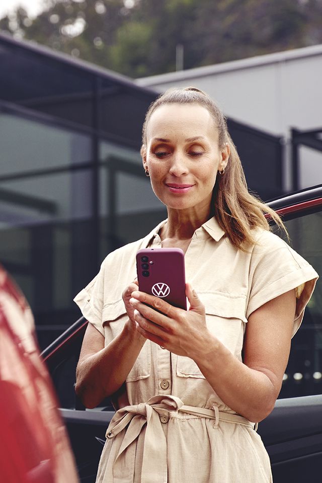 Nő egy VW modell mellett nézi a telefonját