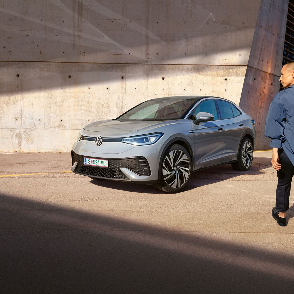 Grauer VW ID.5 parkt vor heller Hauswand, Ansicht schräg rechts von vorn, Mann geht zügig auf das E-Auto zu.