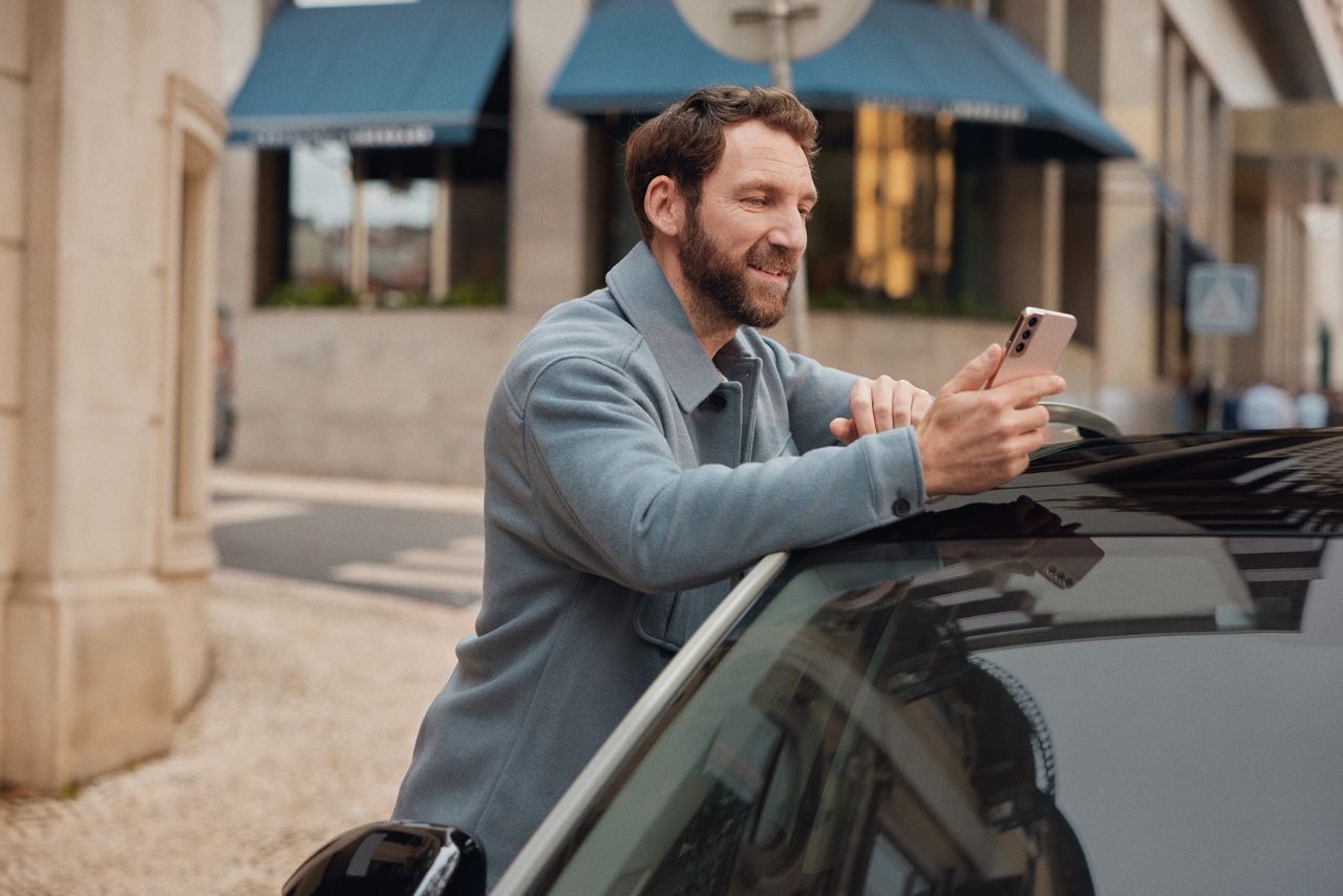 férfi az autónak támaszkodik okostelefonnal a kezében