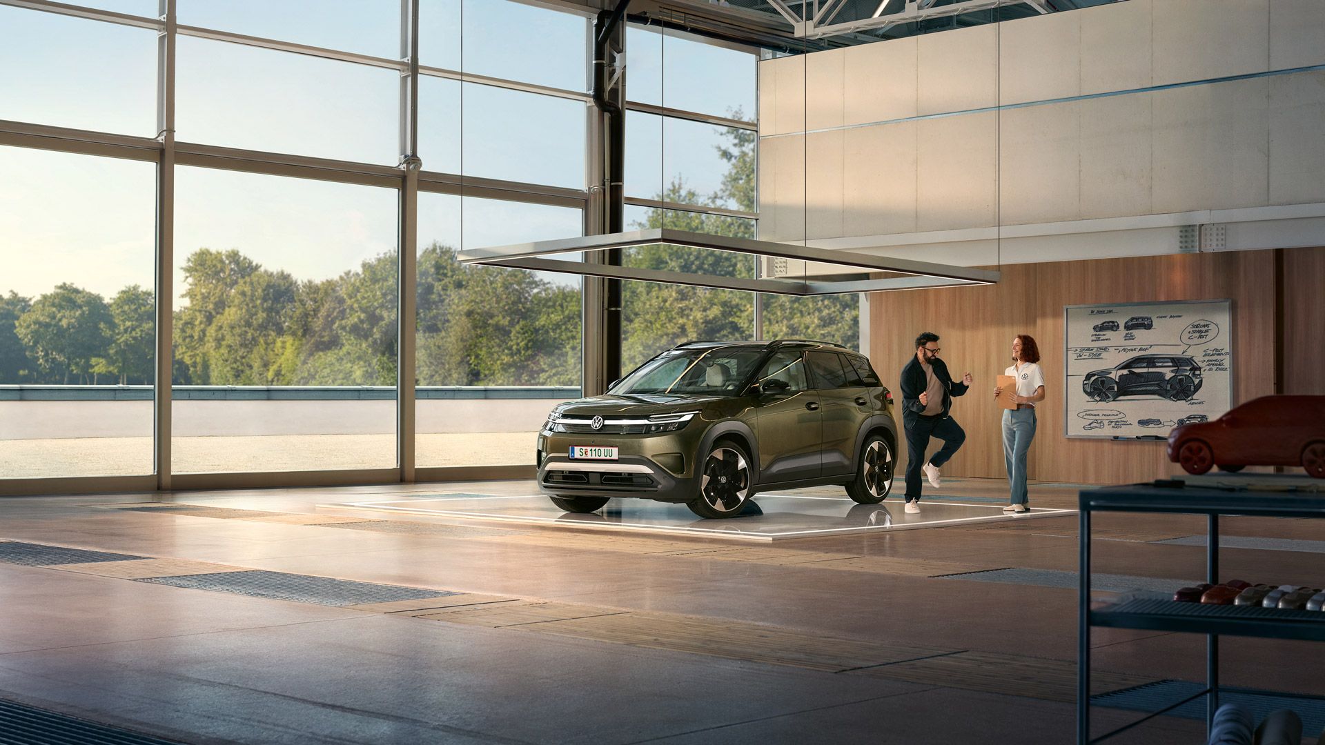Egy VW ID. Cross áll egy minimalista berendezésű dizájnstúdióban, mellette egy izgatott férfi táncolgat, és egy mérnöknővel beszélget.