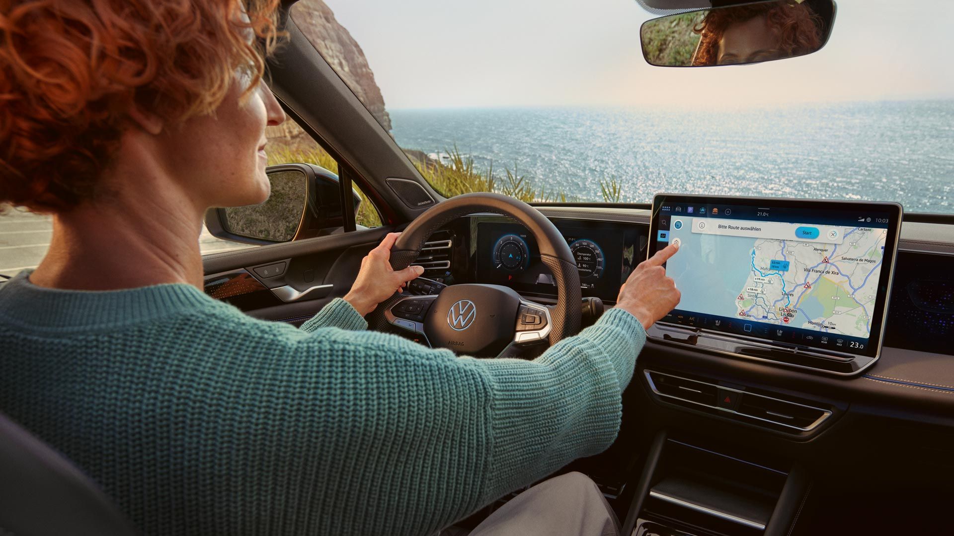 Eine Frau sitzt in ihrem neuen Tiguan und stellt auf ihrem 15 Zoll Display die Navigation ein.