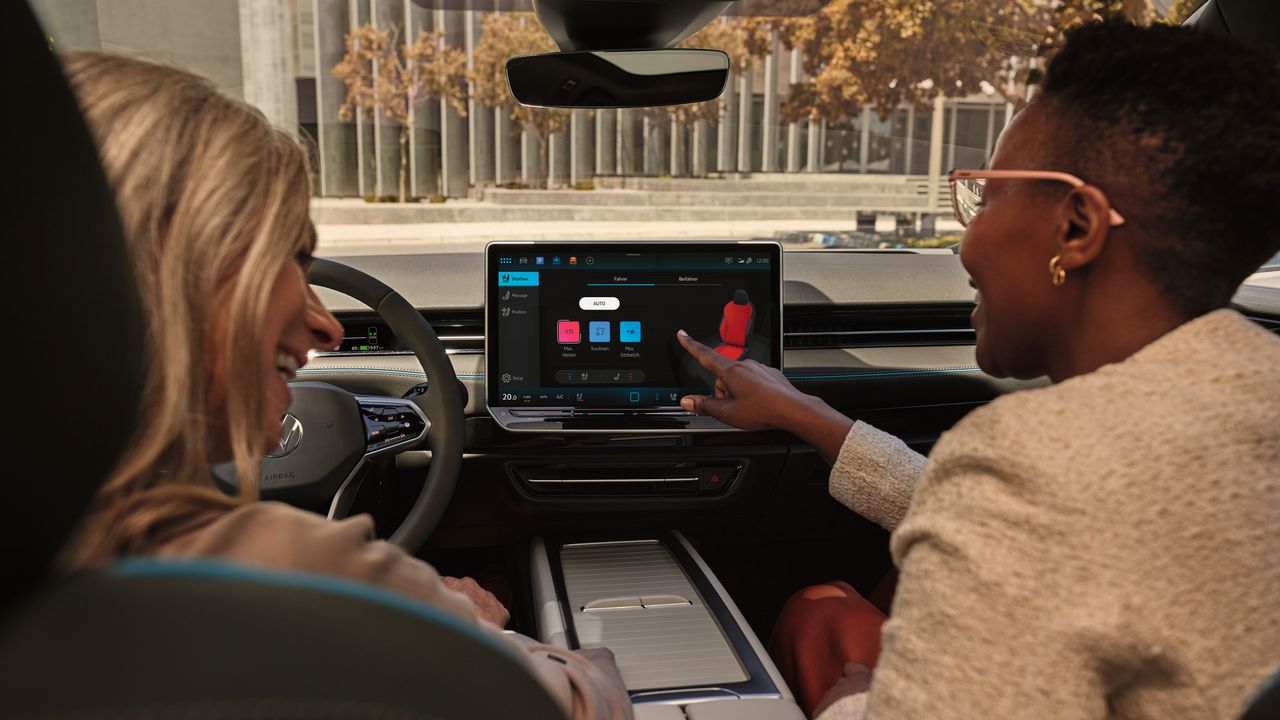 Zwei Frauen sitzen im ID.7 und bedienen die Sitzheizung über das Touchdisplay des Infotainmentsystems