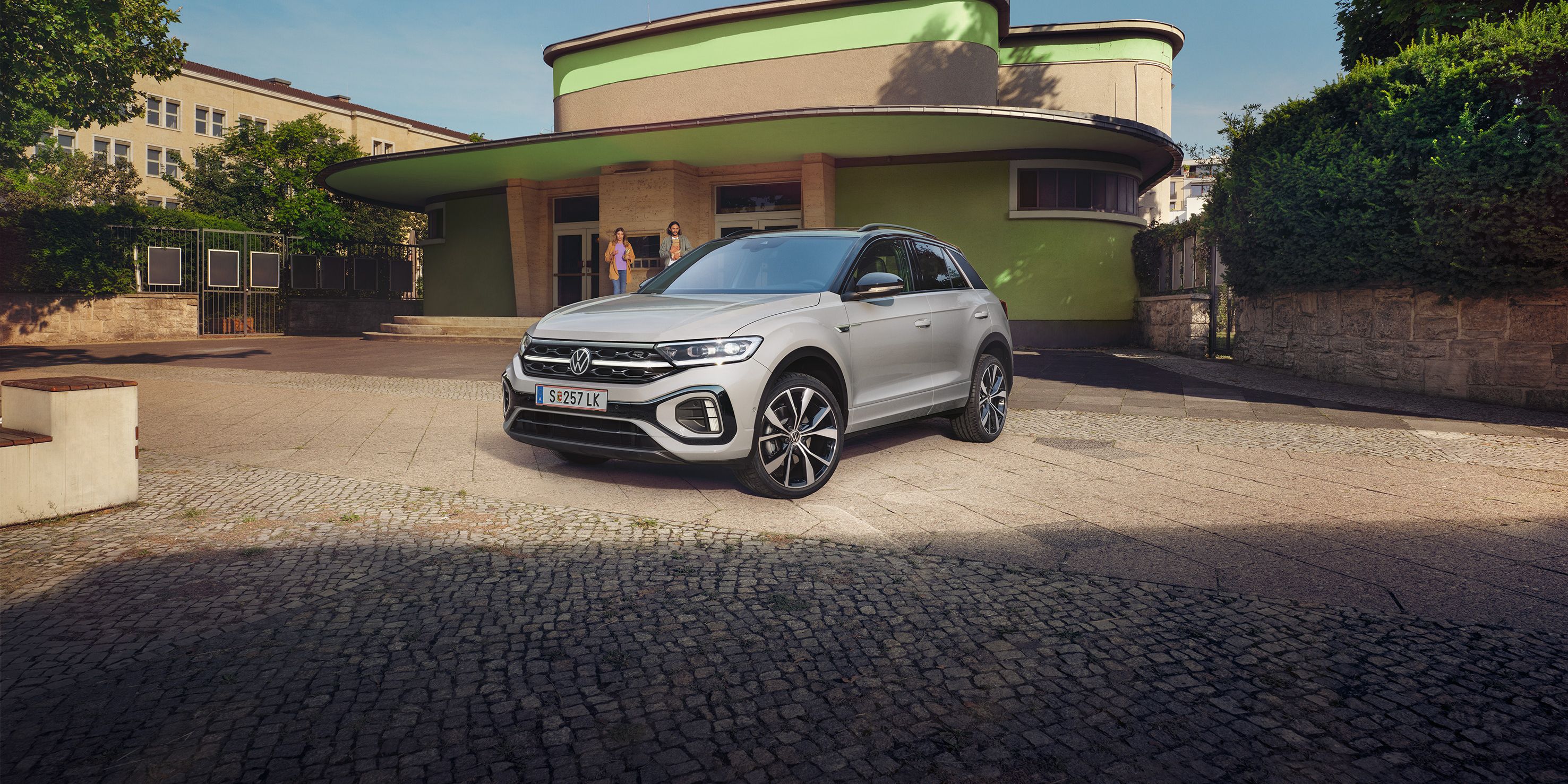 VW T-Roc R-Line in weiß vor einem Gebäude, Front und Seite sichtbar