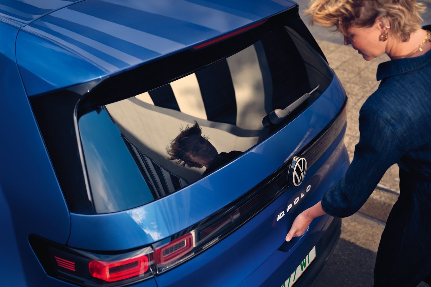 Eine Frau öffnet die Kofferraumklappe eines blauen VW ID. Polo Style.