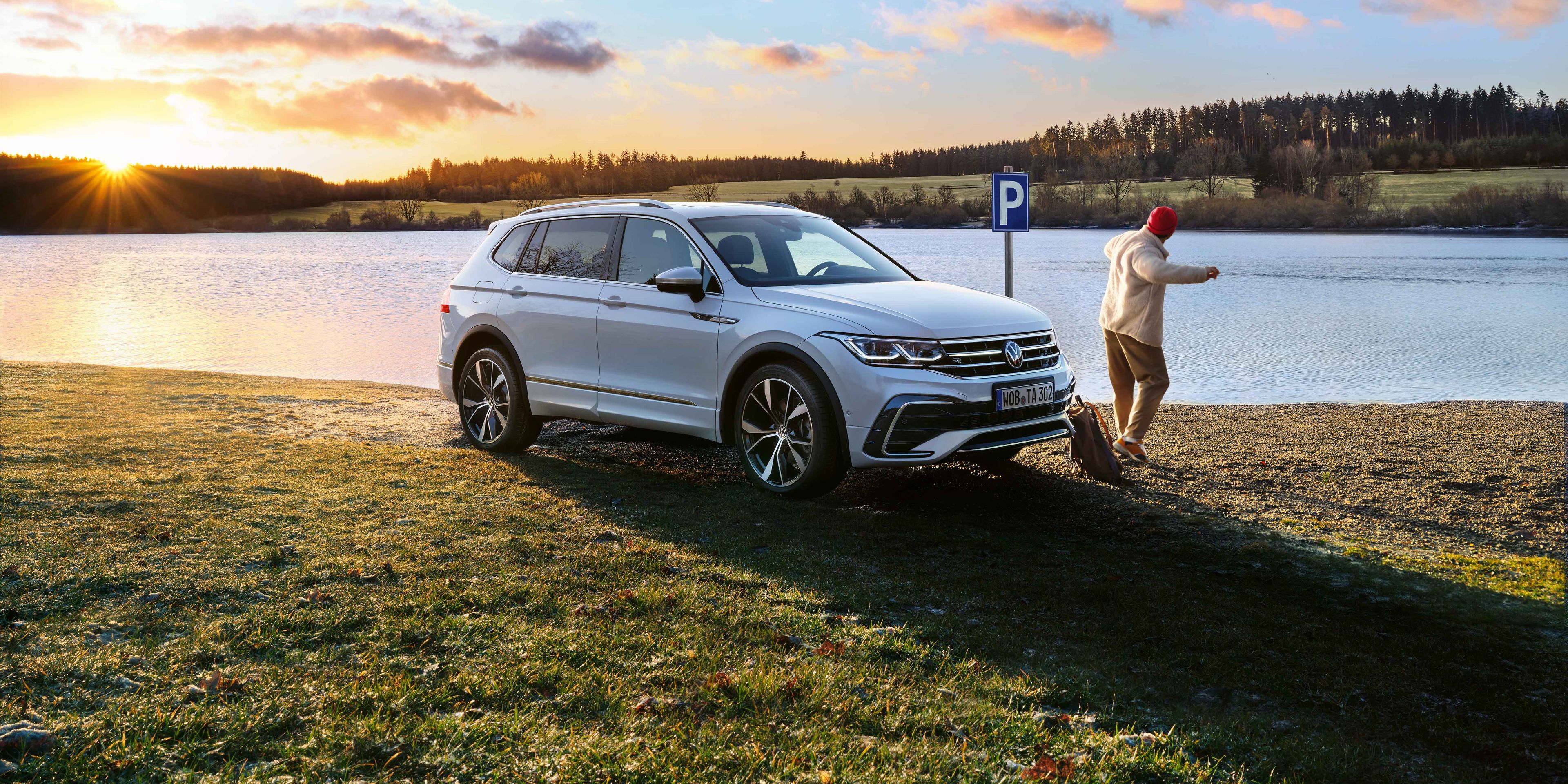 Ein weißer Tiguan Allspace R-Line mit getönten Heckscheiben und angeschalteter Lichtsignatur steht am Seeufer.