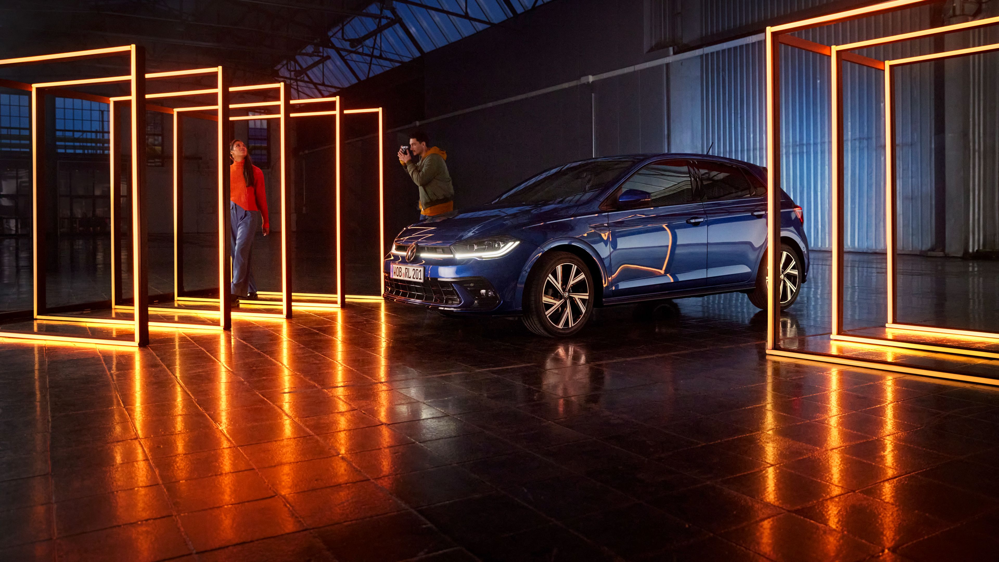 Egy kék VW Polo LED-es világítással és LED-mátrix fényszórókkal áll egy sötét teremben, téglalap alakú fényelemekkel körülvéve.