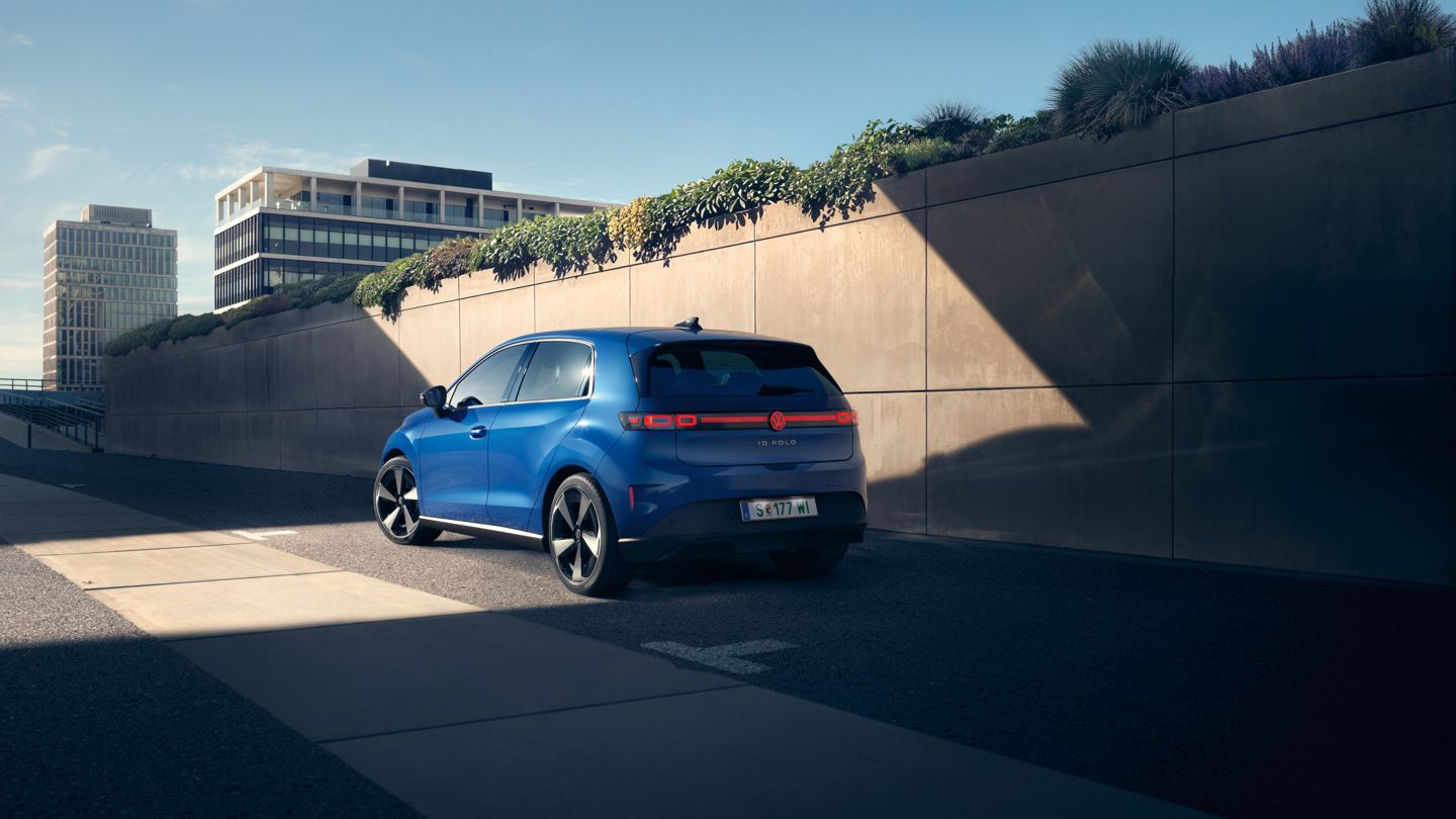 Egy kék VW ID. Polo az út szélén áll egy növényzettel borított fal előtt, és egy férfi odasétál hozzá.