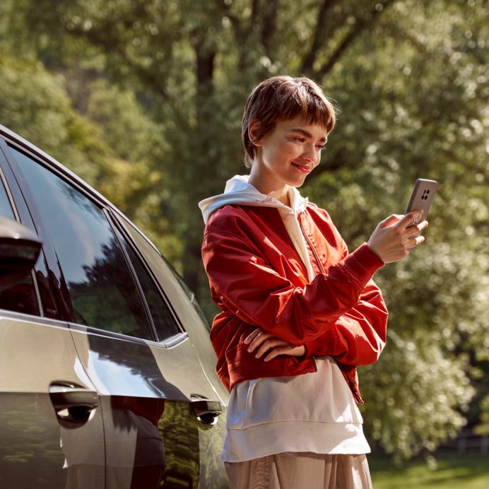 nő egy okostelefonnal áll egy VW modell mellett
