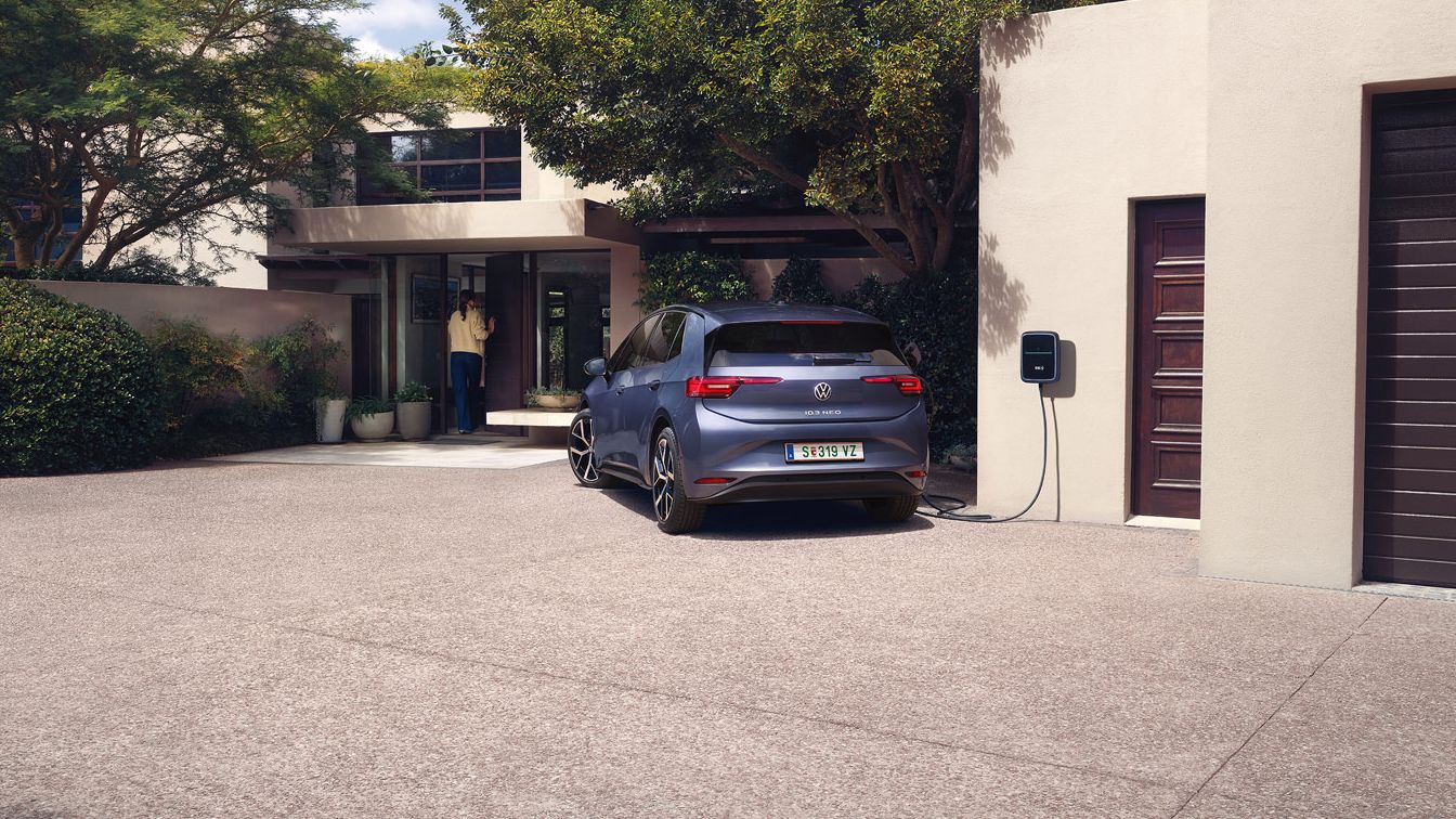 Egy kék VW ID.3 Neo tölt egy családi ház előtt, wallboxhoz csatlakoztatva.