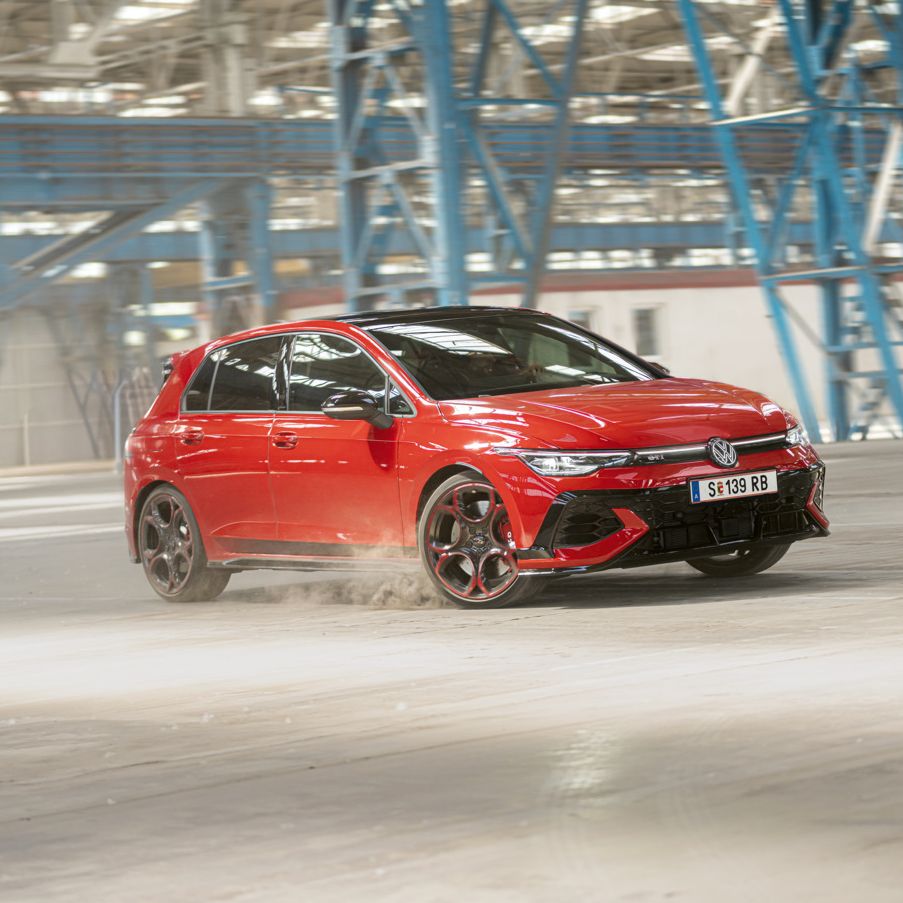 Piros Volkswagen Golf GTI halad gyorsan keresztül egy üres gyárépületben, miközben port kavar a kerekekkel.