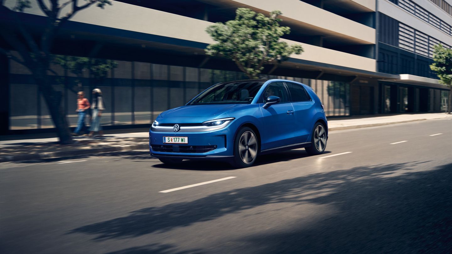 Egy kék VW ID. Polo halad egy városban, az út mentén zöldellő fák.