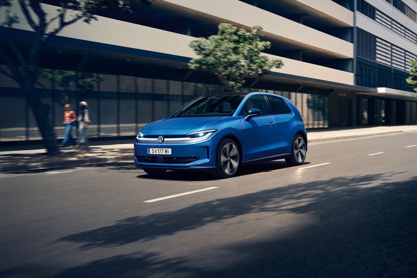 Egy kék VW ID. Polo halad egy városban, az út mentén zöldellő fák.