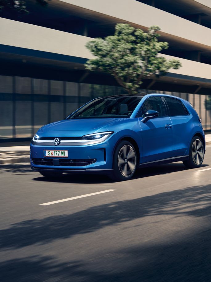 Egy kék VW ID. Polo halad egy városban, az út mentén zöldellő fák.