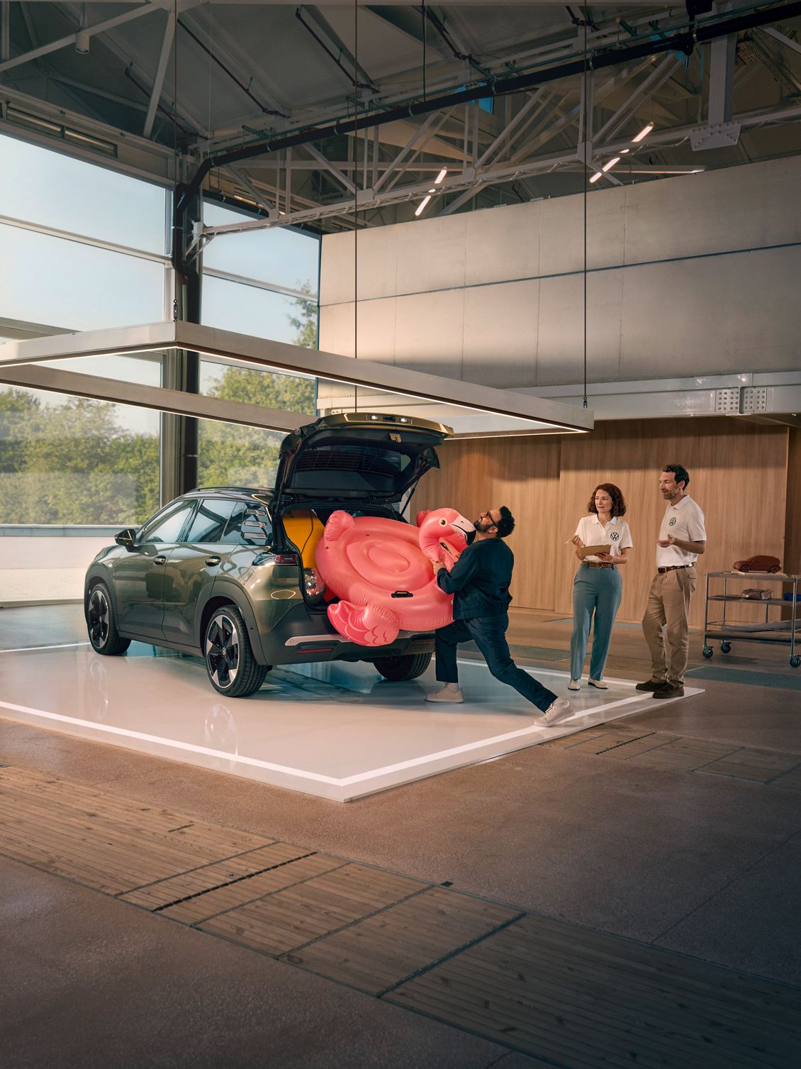 Egy férfi egy felfújható flamingót próbál betuszkolni a VW ID. Cross nyitott csomagterébe. Két személy áll mellette, és jót derülve figyeli.
