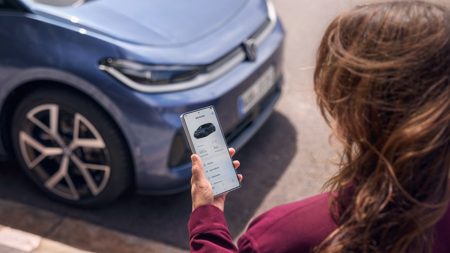 Egy nő az okostelefonjára néz, előtte egy kék VW ID.3 Neo parkol.