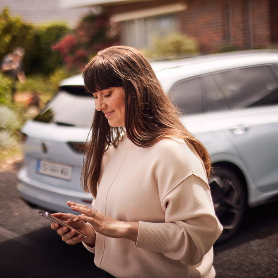 Egy nő nézi a telefonját, háttérben egy VW Golf Variant 