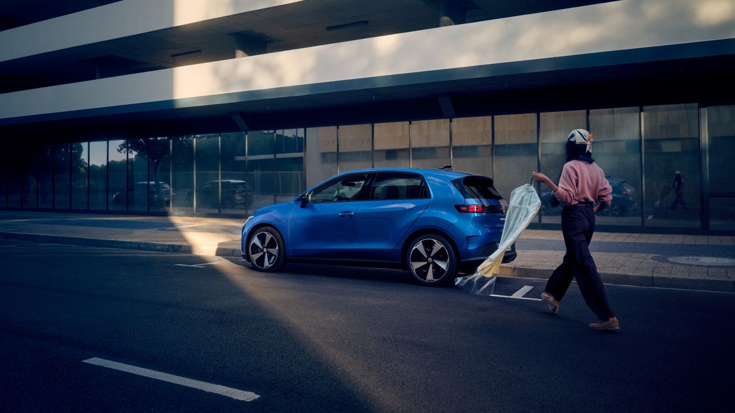 Egy kék VW ID. Polo áll az út szélén párhuzamosan leparkolva, egy nő pedig a jármű felé sétál.