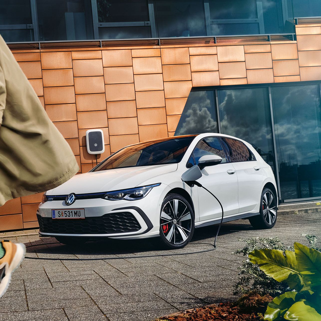 Ein ladender VW Golf GTE hinter dem Anschnitt eines Mannes, der sich grade vom Fahrzeug entfernt. 