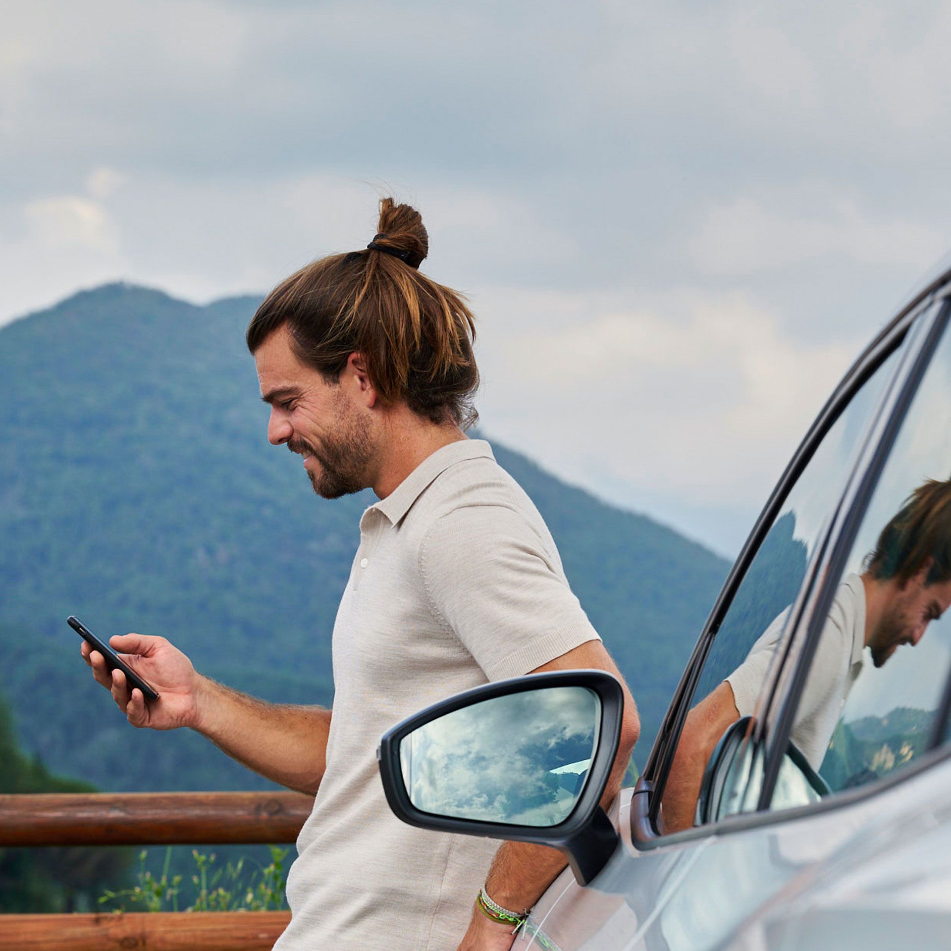 Ein Mann lehnt an einem Volkswagen ID. und blickt auf sein Smartphone.