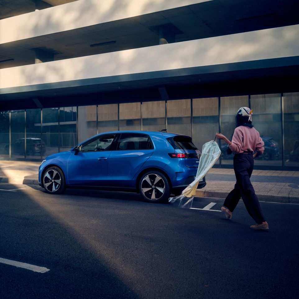 Egy kék VW ID. Polo áll az út szélén párhuzamosan leparkolva, egy nő pedig a jármű felé sétál.