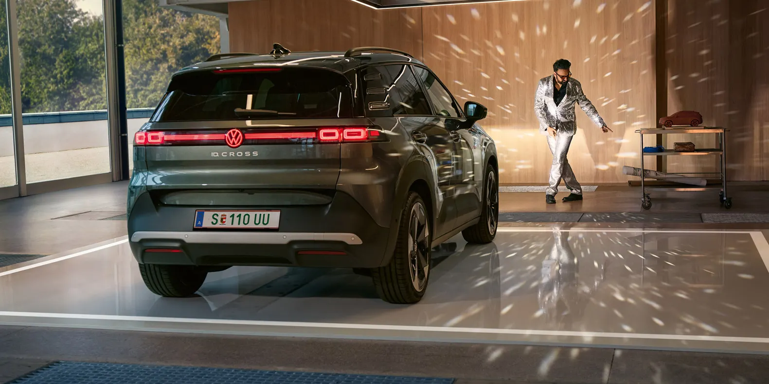 Egy VW ID. Cross bekapcsolt fényszórókkal áll egy csarnokban, és megvilágít egy csillogó öltönyben táncoló férfit.