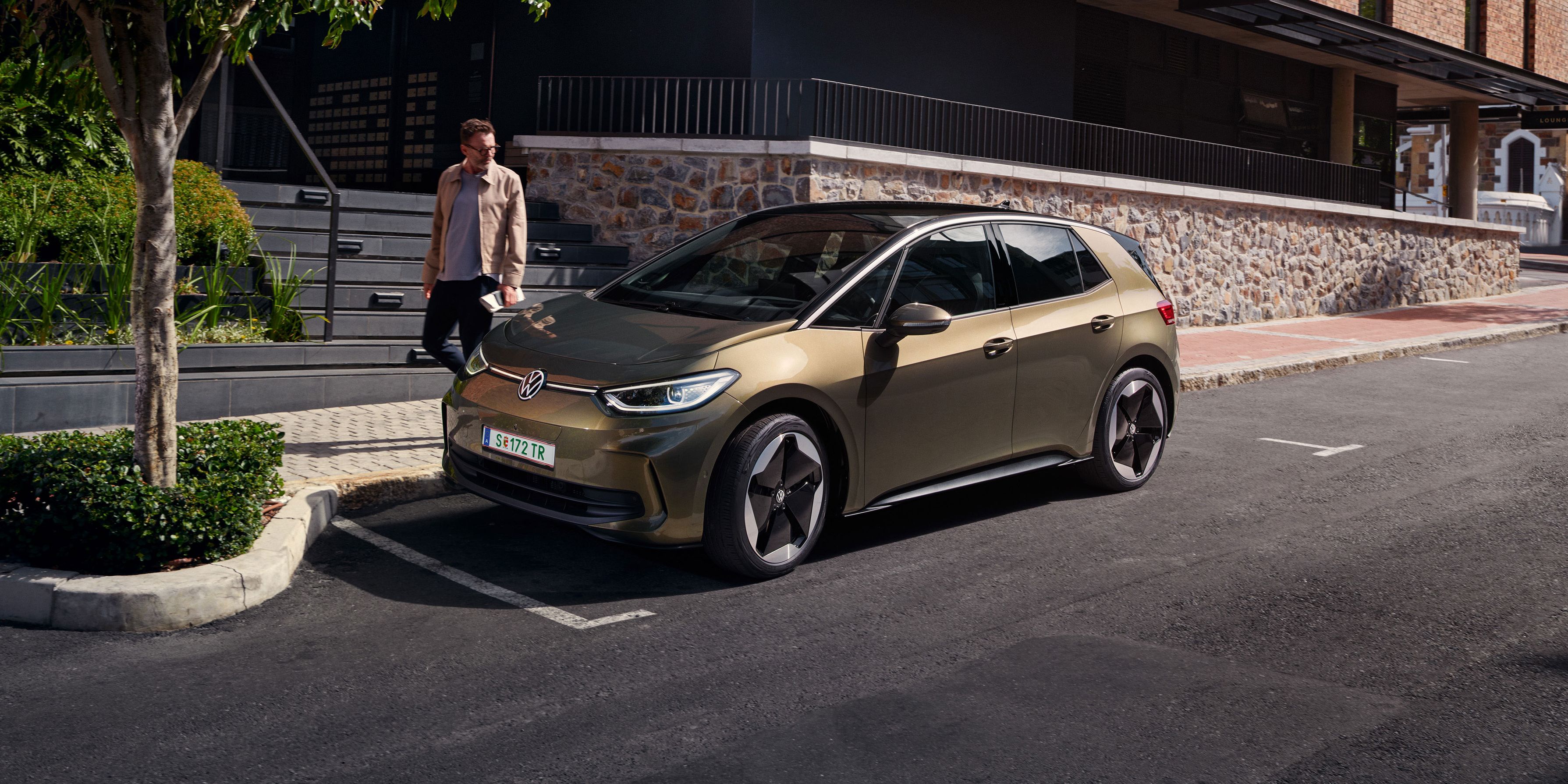 Blick auf einen VW ID.3 in "Dark Olivine Green Metallic", der am Straßenrand am Bordstein parkt.