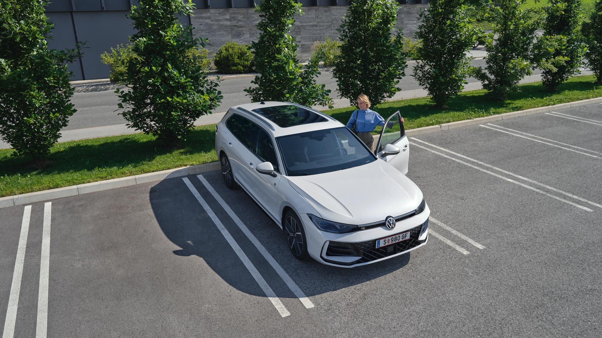 Topshot eines neuen weißen VW Passat auf einem Parkplatz, eine Frau steigt auf der Fahrerseite ein.
