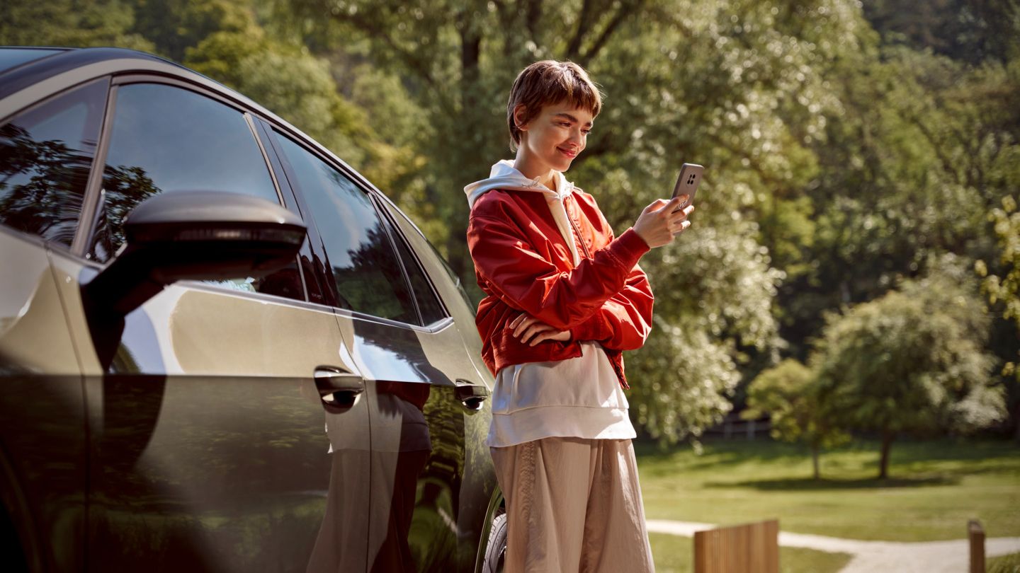 nő egy okostelefonnal áll egy VW modell mellett