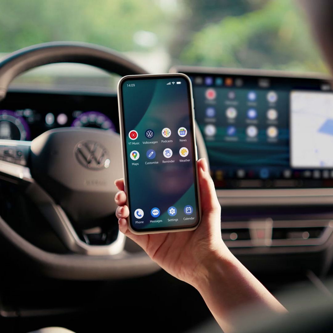 Egy nő ül egy Volkswagen vezetőterében, kezében mobiltelefon.