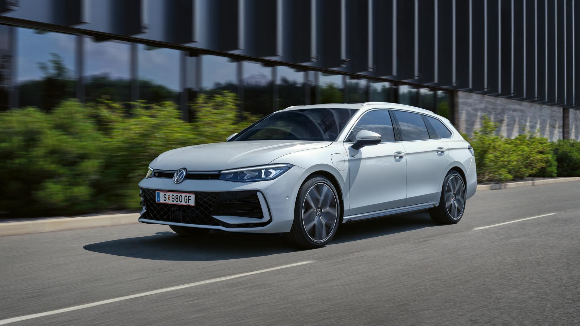 VW Passat in weiß fährt seitlich an einem Gebäude vorbei.