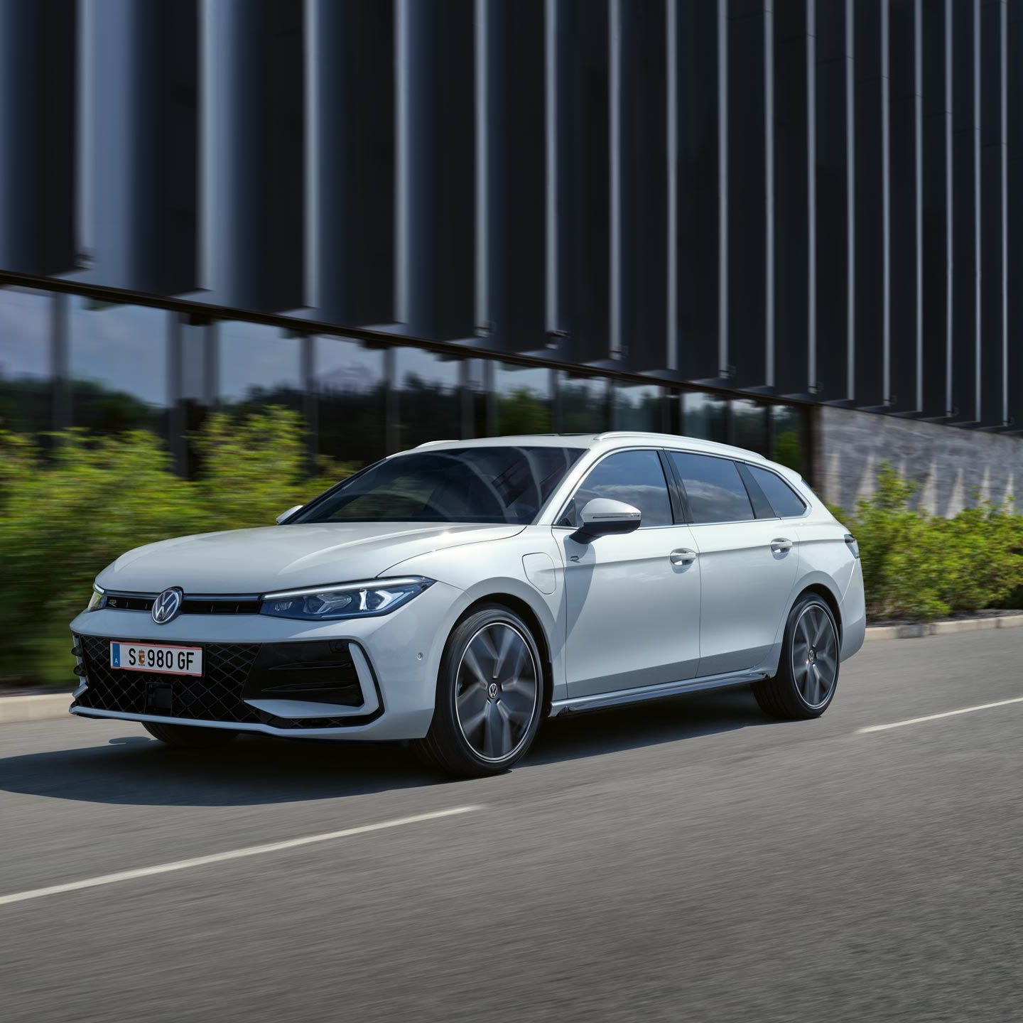 VW Passat in weiß fährt seitlich an einem Gebäude vorbei.