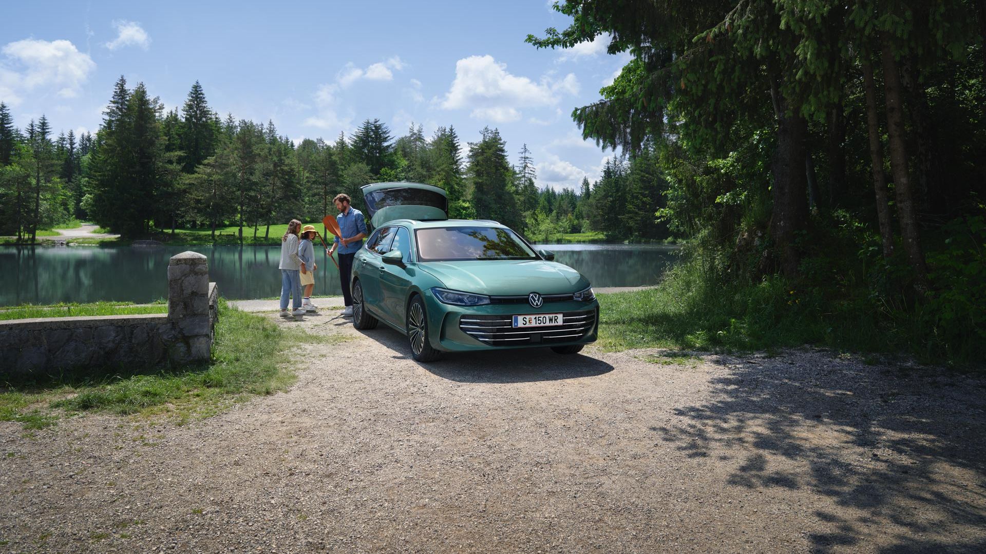 Der neue VW Passat in blaugrün parkt an einem Badesee mit geöffnetem Kofferraum. Ein Mann verteilt Freitzeitspielzeug an zwei Kinder.