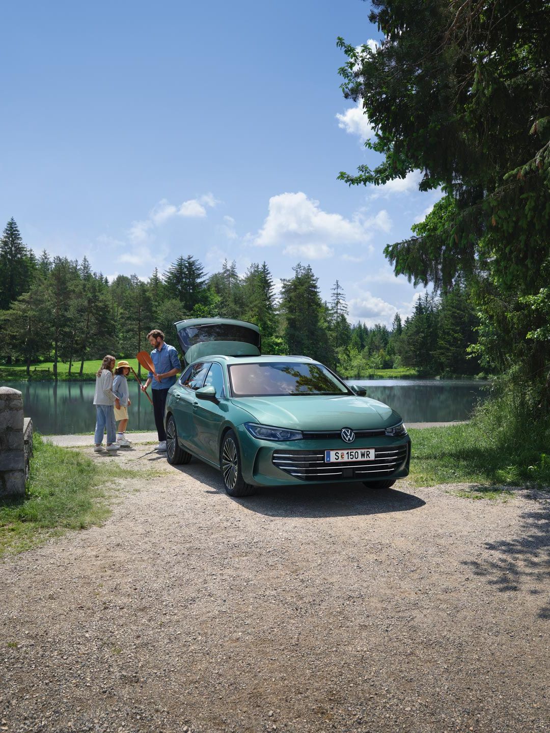 Der neue VW Passat in blaugrün parkt an einem Badesee mit geöffnetem Kofferraum. Ein Mann verteilt Freitzeitspielzeug an zwei Kinder.