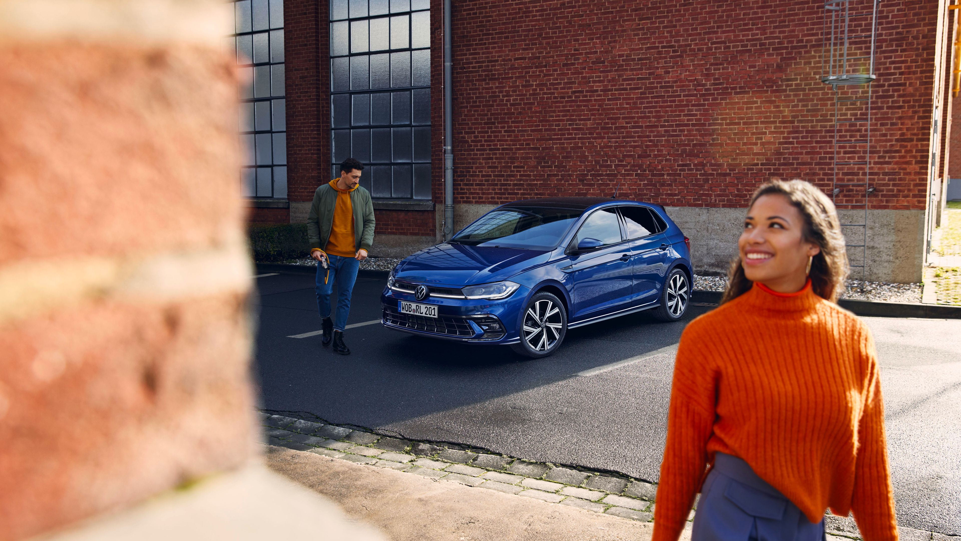 Egy kék VW Polo parkol egy parkolóban, előtte egy férfi áll és a motorháztetőt nézi.