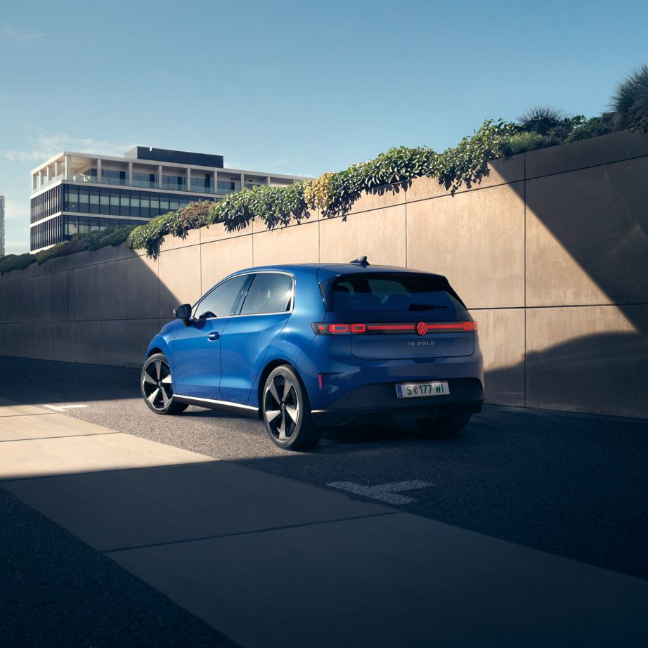 Egy kék VW ID. Polo az út szélén áll egy növényzettel borított fal előtt, és egy férfi odasétál hozzá.