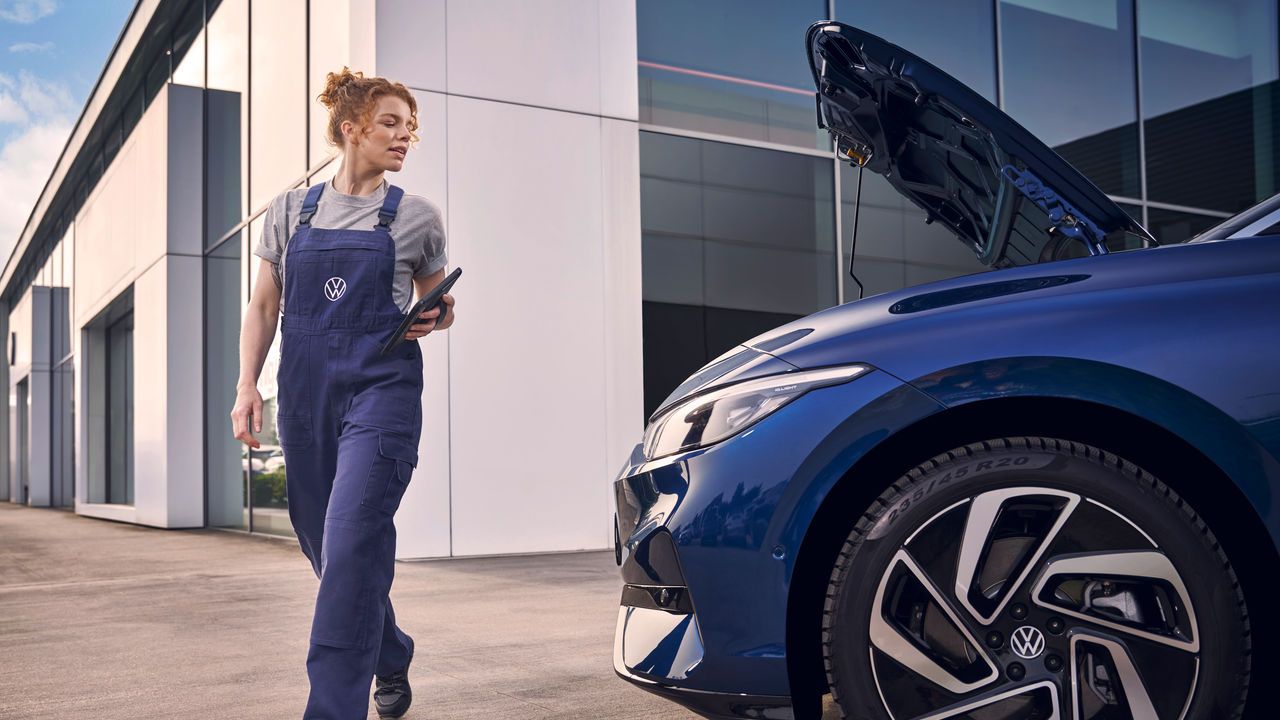 Eine Volkswagen Technikerin mit Tablet begutachtet einen blauen ID.7 