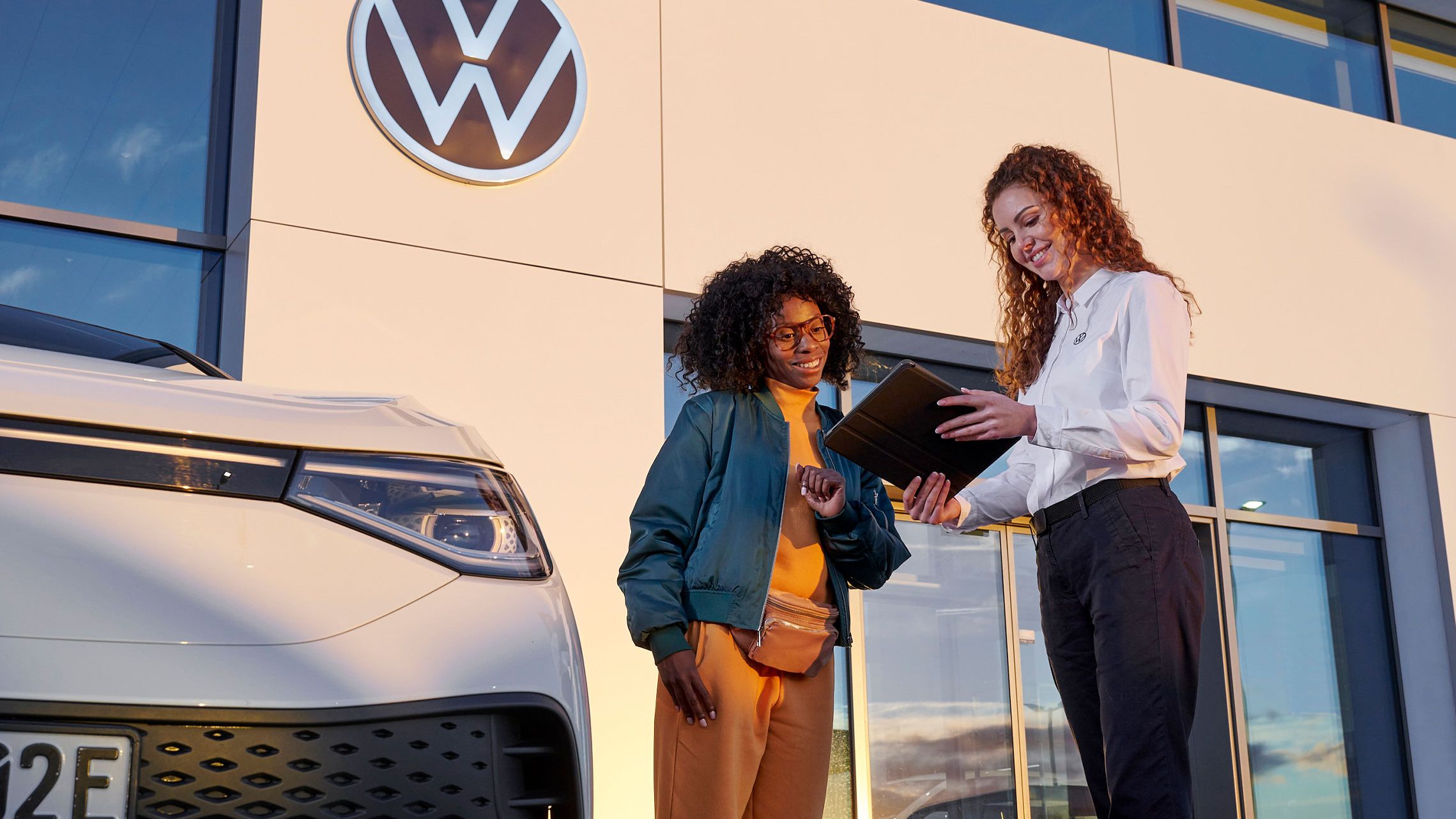 Eine VW Service MItarbeiterin mit einer Kundin vor einem Volkswagen Servicebetrieb