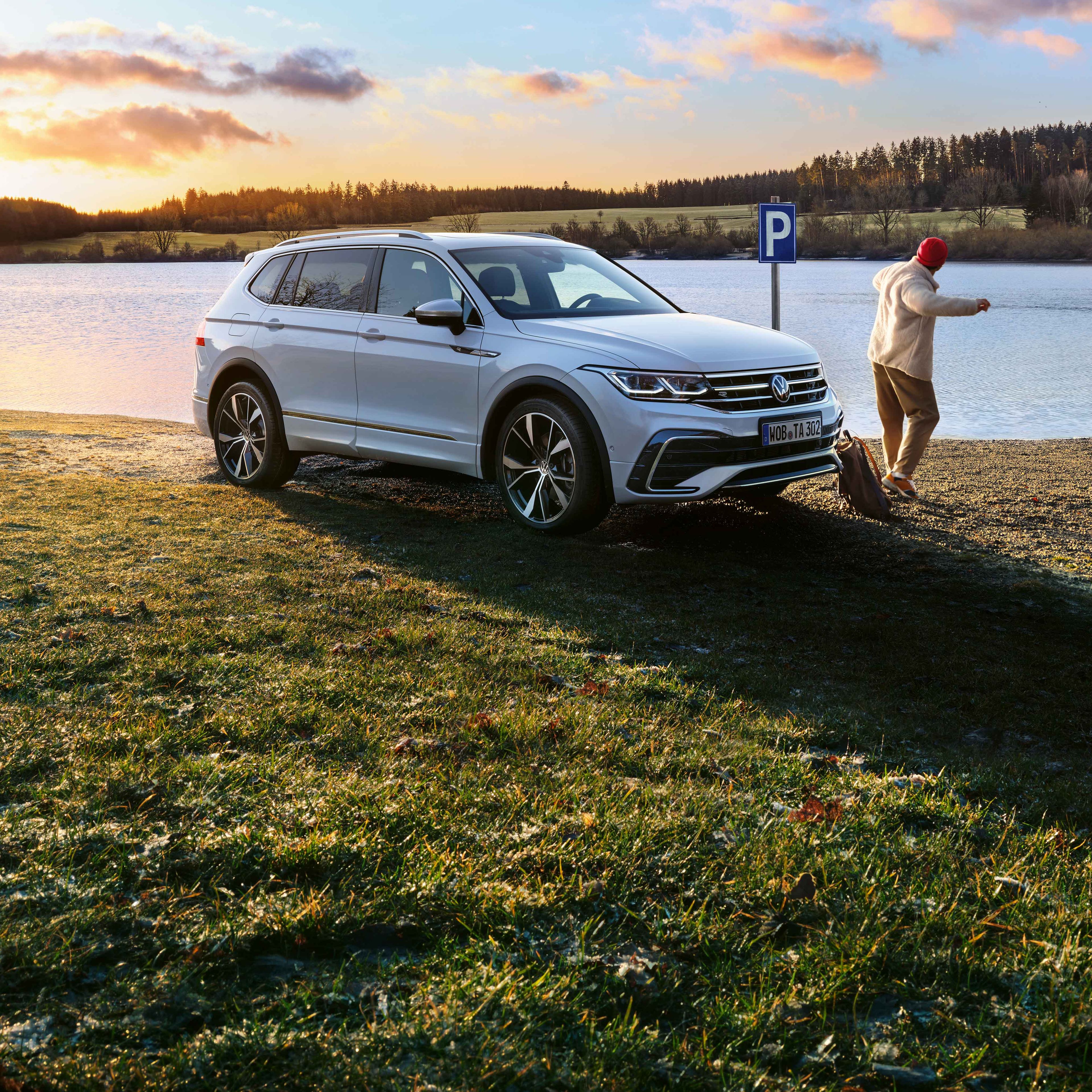 Ein weißer Tiguan Allspace R-Line mit getönten Heckscheiben und angeschalteter Lichtsignatur steht am Seeufer.
