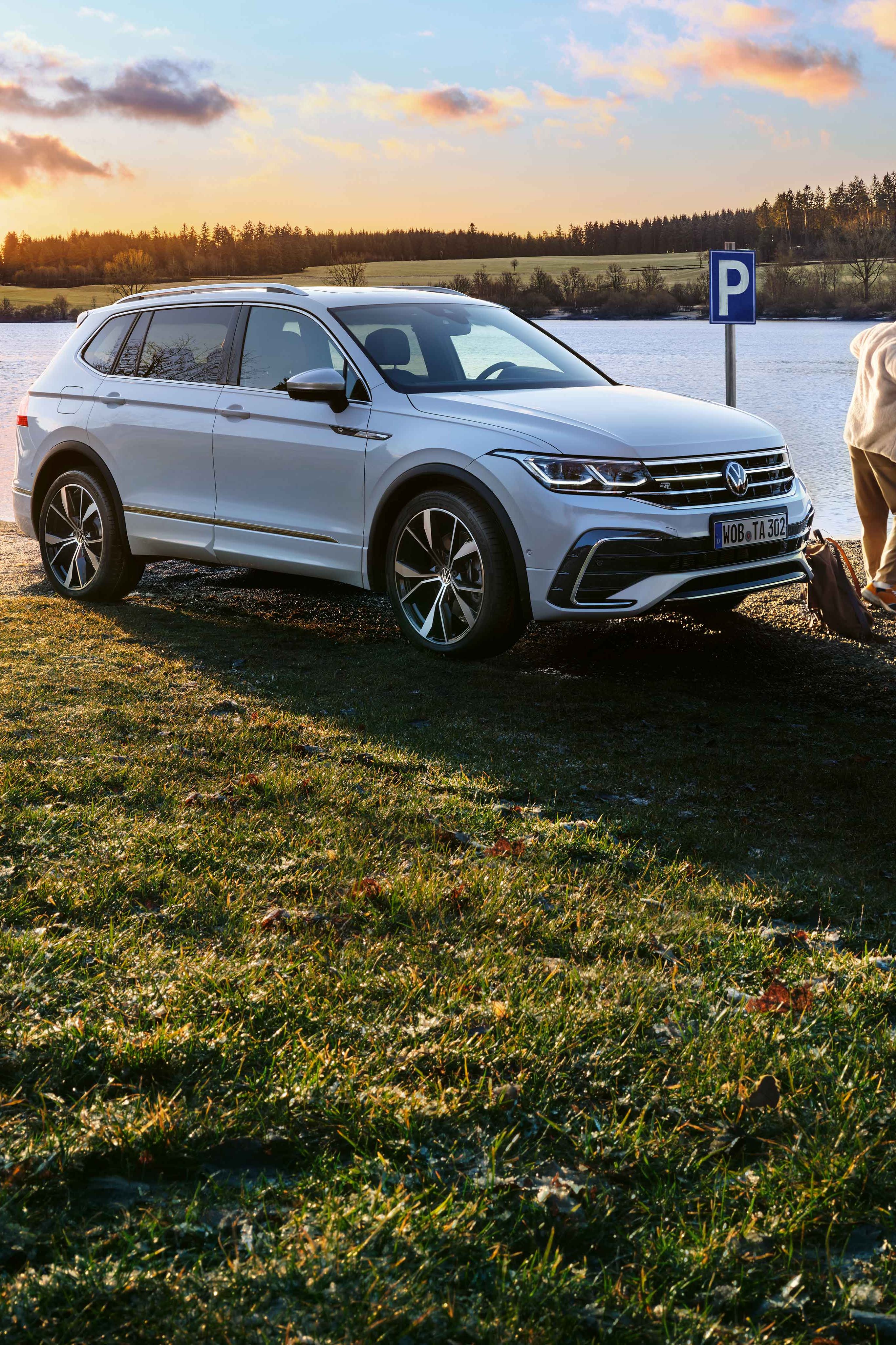 Ein weißer Tiguan Allspace R-Line mit getönten Heckscheiben und angeschalteter Lichtsignatur steht am Seeufer.